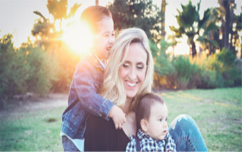 Mother and young sons embracing on a lawn at sunset